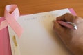 Top view of female hands writing in breast cancer awareness files folder, copy space with pink ribbon