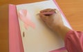 Top view of female hands writing in breast cancer awareness files folder, copy space with pink ribbon