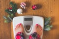 Top view of female legs in pajamas on a white weight scale with Christmas decorations and lights on wooden background Royalty Free Stock Photo