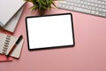 Top view of female workspace with digital tablet, notebook, house plant and keyboard on pink background.