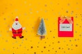 Top view festive composition with Santa Claus, Christmas tree and gift card on bright yellow background with sparkle stars. Royalty Free Stock Photo