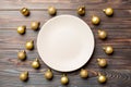 Top view of festive plate with golden baubles on wooden background. Christmas decorations and toys. New Year advent concept Royalty Free Stock Photo