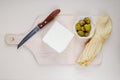 top view of feta cheese with string cheese , pickled olives and kitchen knife on a wooden cutting board on white background Royalty Free Stock Photo