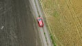 Top view of a field with wheat and a red car moving on the rural road.