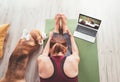 Top view at fit sporty healthy woman sitting on yoga mat, watching online yoga class on laptop computer and petting her beagle dog Royalty Free Stock Photo