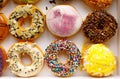 Top view flat lay of a colorful group of twelve delicious donuts in a white paper box on a wooden table. Collection of dozen