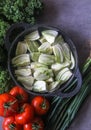 Top view, flat lay of fresh cut Florence fennel bulbs arranged in a dark pot, with Kyle, ripe tomatoes and spring onion