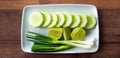 Top view of flat lay of fresh Scallion, sliced cucumber and lime or lemon in white plate on wooden table Royalty Free Stock Photo