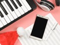 Mobile phone , blank music sheet , Christmas Santa hat, headphones and  electric piano on pink background with copy space.Remote Royalty Free Stock Photo