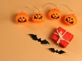 Flat lay of red gift box with black paper bats and Halloween pumpkin lights on orange background with copy space. Halloween