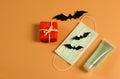 Flat lay of red gift box with black paper bats , medical face mask and alcohol sanitizer gel  on orange background with copy space Royalty Free Stock Photo