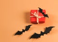 Flat lay of red gift box with black paper bats on orange background with copy space. Halloween present concept