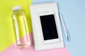 smartphone,water bottle and notebook on blue,pink and yellow vibrant background