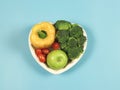 Flat lay of vegetables capsicum, broccoli tomatoes and green apple in heart shape plate on blue background with copy space,