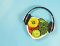 Flat lay of vegetables and fruit in heart shape plate, with headphones around on blue background with copy space Royalty Free Stock Photo