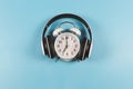 Flat lay of vintage alarm clock show 7 o`clock cover with headphones on blue background ,time to listen to music concept or