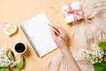 Top view, flat lay women desk with lilac flowers, silk scarf, coffee cup, gift box, human hand holding golden pen and writing in Royalty Free Stock Photo