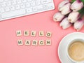 Flat lay of wooden letter HELLO MARCH on pink background with coffee cup, computer keyboard and purple-white tulip bouquet Royalty Free Stock Photo