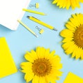 Top view flat lay of workspace desk styled design with sunflowers, white paper bag pencils pen notebook diary paper clips on blue Royalty Free Stock Photo