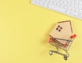 flat layout of wooden house model in shopping trolley and and computer keyboard on yellow background with copy space, home Royalty Free Stock Photo