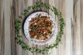 Top view of flatbread with meat on a round plate decorated with greens on a wooden table