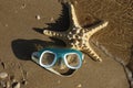 Top view of foaming waves hitting a swimming mask and a starfish lying on a sandy beach. Vacation on the seashore. Sunny weather. Royalty Free Stock Photo