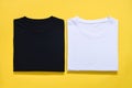 Top view of folded black and white color t-shirt on yellow background, copy space, flat lay