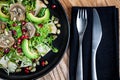 Green vegetarian salad lunch with avocado, artichokes, pomegranate seeds on dark plate.