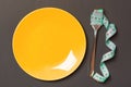 Top view of fork with measure tape near round plate on black background. Weight loss concept with empty space for your idea Royalty Free Stock Photo