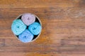 Top view of four cotton balls in blue, mint, turosque and beige colors, assorted in small basket on brown wooden texture with much