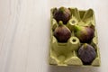 Top view of four figs in yellow egg carton, on white wooden table, in portrait,