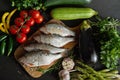 Top view offresh raw dorada fish on a wooden board with a set of vegetables on a black table Royalty Free Stock Photo