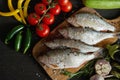 Top view offresh raw dorada fish on a wooden board with a set of vegetables on a black table Royalty Free Stock Photo
