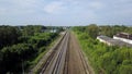 Top view of rows of long railways layng along green line of bushes and trees