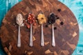 Top view of four spoons with cereal, dry fruits, and granola on a wooden board