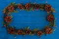 Top view on frame from Christmas lights, fir branches and pine cones on the blue wooden background. Royalty Free Stock Photo