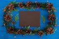 Top view on frame from Christmas lights, fir branches, pine cones and brown sheet of paper on the blue wooden background. Royalty Free Stock Photo