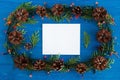 Top view on frame from Christmas lights, fir branches, pine cones and white sheet of paper on the blue wooden background. Royalty Free Stock Photo