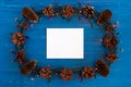 Top view on frame from Christmas lights, pine cones and white sheet of paper on the blue wooden background. Royalty Free Stock Photo