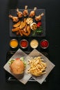 top view of french fries with delicious burger on tray, assorted sauces and slate board with roasted potatoes, grilled vegetables Royalty Free Stock Photo