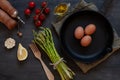 Top view of fresh asparagus, olive oil, tomatoes, lemon, garlic and three eggs on Cast iron pan on black table Royalty Free Stock Photo