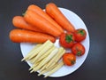 Top view of fresh carrots, Tomato and baby corn on white plate on wooden table Royalty Free Stock Photo