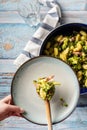 Top view on fresh prepared broccoli with gnocchi in casserole dish on the wooden table - hand of unknown person putting homemade