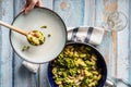 Top view on fresh prepared broccoli with gnocchi in casserole dish on the wooden table - hand of unknown person putting homemade