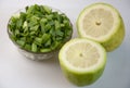 Top view of fresh raw chopped green onions in a bowl and lemons on a white background