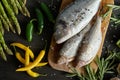 Top view of fresh raw dorada fish on a wooden board with a set of vegetables on a black table Royalty Free Stock Photo