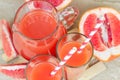 Top view of fresh red grapefruit juice in a glass with a straw and jar with fruit pieces on light wooden background. Royalty Free Stock Photo