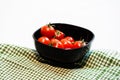 Top view of fresh ripe cherry tomatoes in small black bowl on a rustic white wooden table. Ingredients and food concept Royalty Free Stock Photo