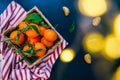 Top view Fresh ripe mandarins, clementine, tangerine with green leaves in the straw bowl on a striped napkin and dark