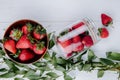 top view of fresh ripe strawberries in a wooden bowl and strawberries scattered from a glass jar and green leaves on white wooden Royalty Free Stock Photo